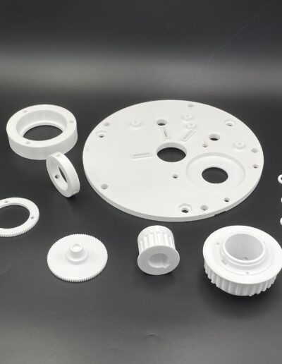 3D printed parts for an educational installation, including gears and mechanical components, produced using FDM technology in white PETG material